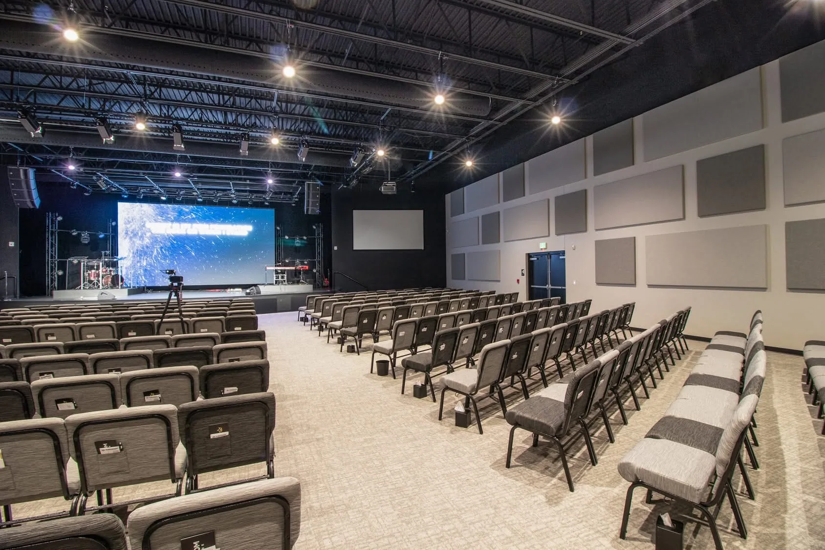 Auditorium with a stage, rows of seating and acoustic wall panels.